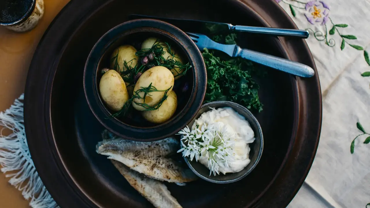 En rustik tallrik med nykokt färskpotatis, stekt fisk och en krämig sås. En härlig bit av finsk mat, redo att avnjutas.