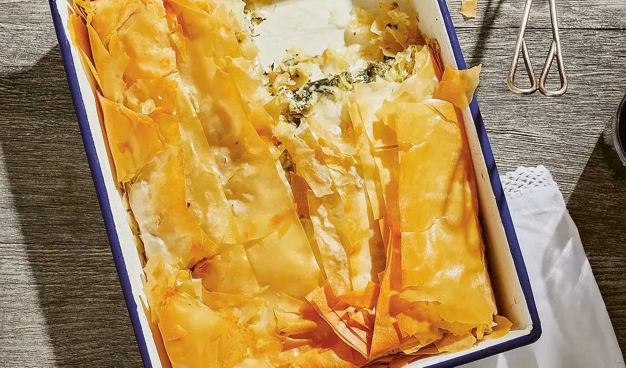 En gyllene, krispig spenatpaj i en blå kantad form. Perfekt för ett spanakopita recept.