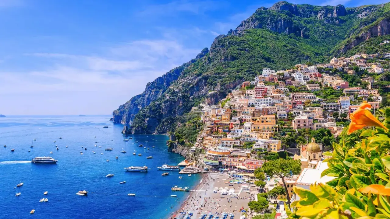Färgglada hus klättrar uppför bergssluttningen vid en livlig strand och blått hav. En vacker vy som ger fakta om Italien.