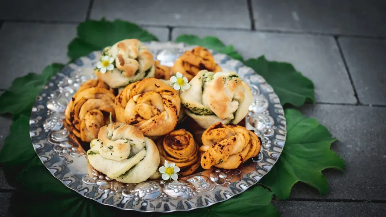 En silverbricka fylld med vackert formade vegetariska pizzabullar, dekorerade med små vita blommor och gröna blad.
