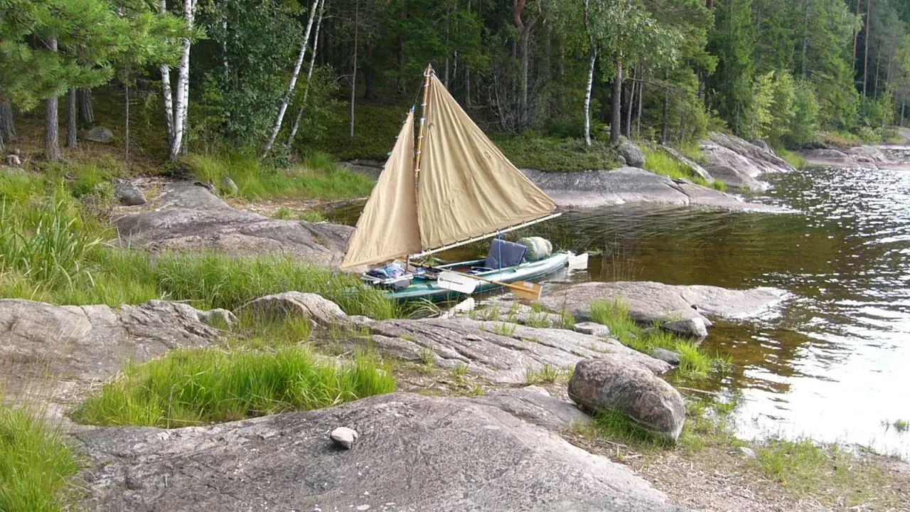 En liten segelbåt med åror ligger vid en stenig strand. En härlig plats att paddla Dalslands kanal på.