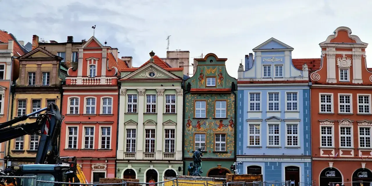 Färgglada husfasader i **Poznan, Polen**, med detaljerade ornament och tak. En byggkran syns i förgrunden.