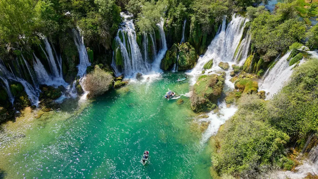 Vackra Kravice vattenfall med turkost vatten och båtar som glider fram. En idyllisk plats för avkoppling.