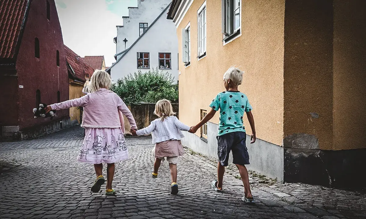 Tre barn håller varandra i handen på en kullerstensgata på Gotland, på väg mot äventyr.