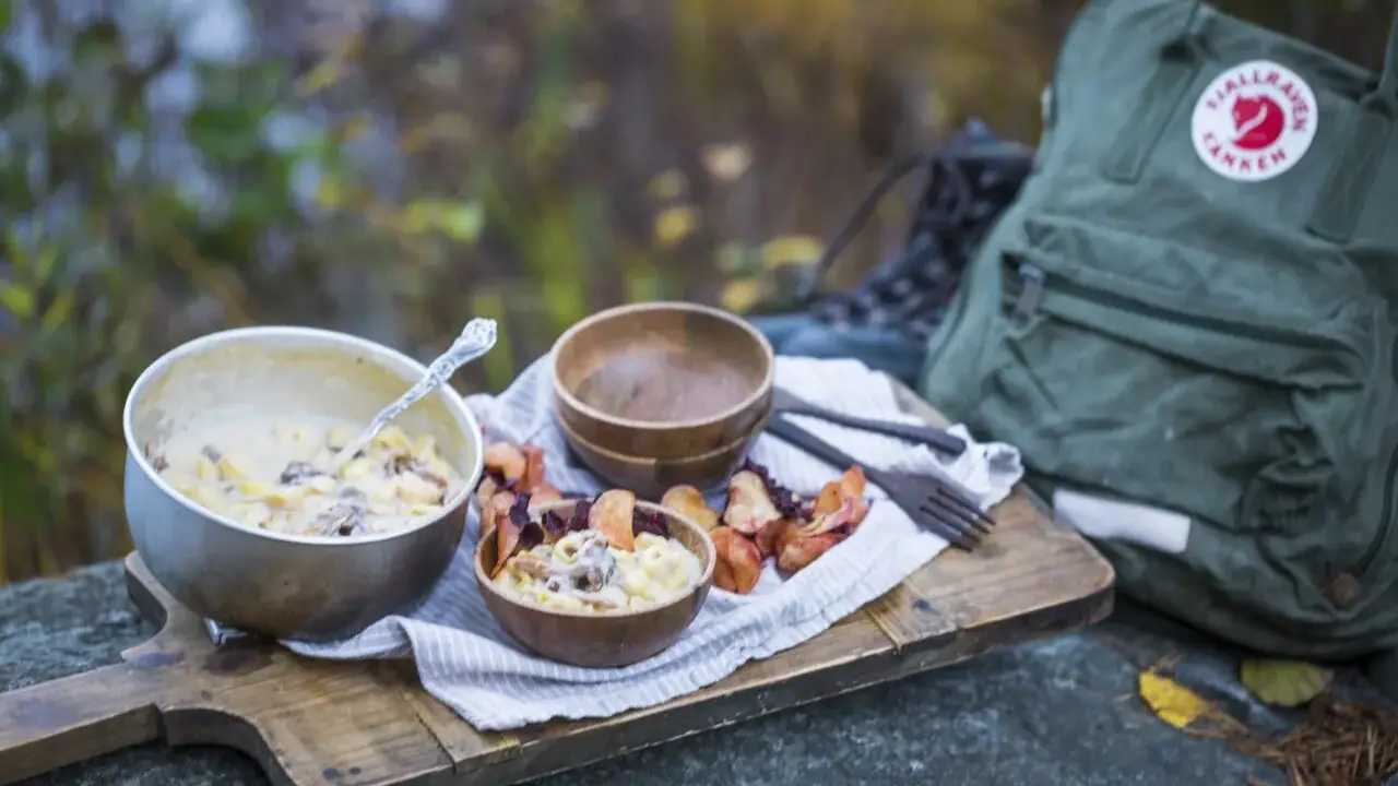 En härlig måltid med pasta och svamp, perfekt för att torka kyckling och njuta av naturen. En Fjällräven ryggsäck och vandringskängor syns i bakgrunden.