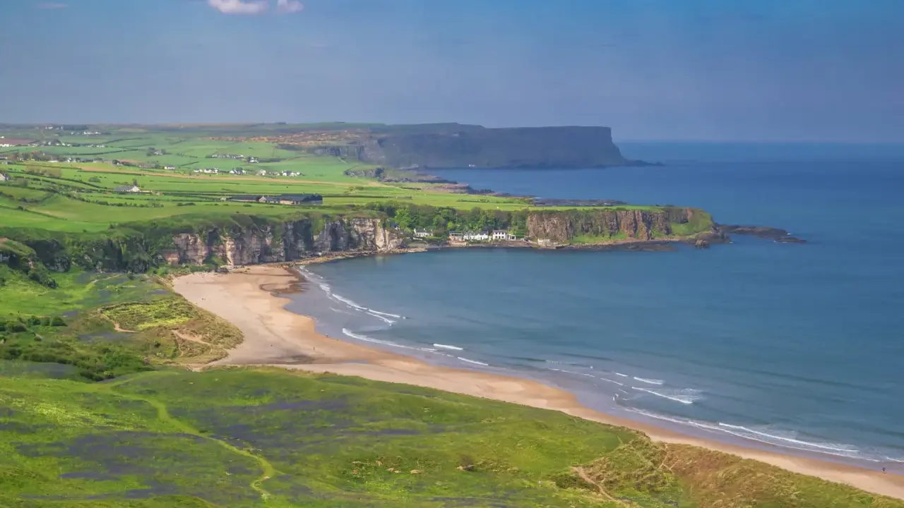 Grönskande kullar och en sandstrand vid havet på Irland, nära Belfast.
