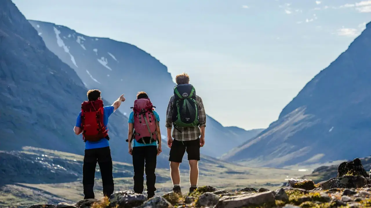 Två vandrare med ryggsäckar blickar ut över en dal under en kungsleden vandring. En pekar mot bergen.
