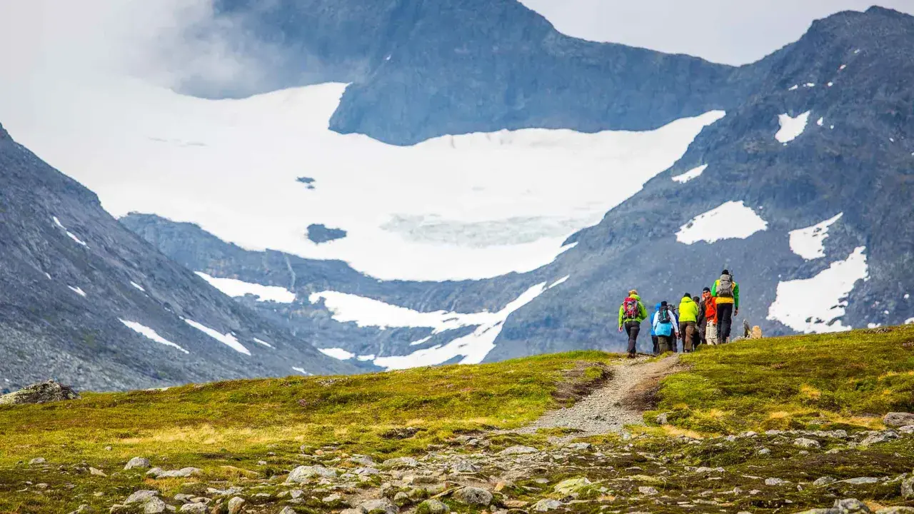 Vandringsgrupp på väg uppför en stenbelagd stig mot Sylarnas glaciärklädda toppar.