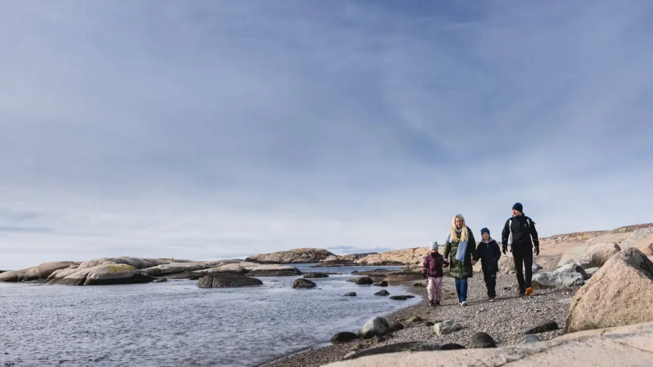 Familj promenerar längs en stenig strand vid Tjurpannans naturreservat.