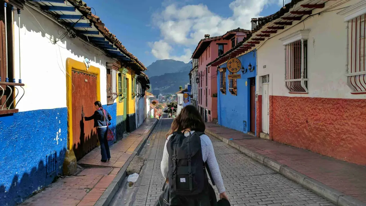 Färgglada hus i La Candelaria, Bogotá. En kvinna med ryggsäck går längs en kullerstensgata. Här finns fakta om Colombia.