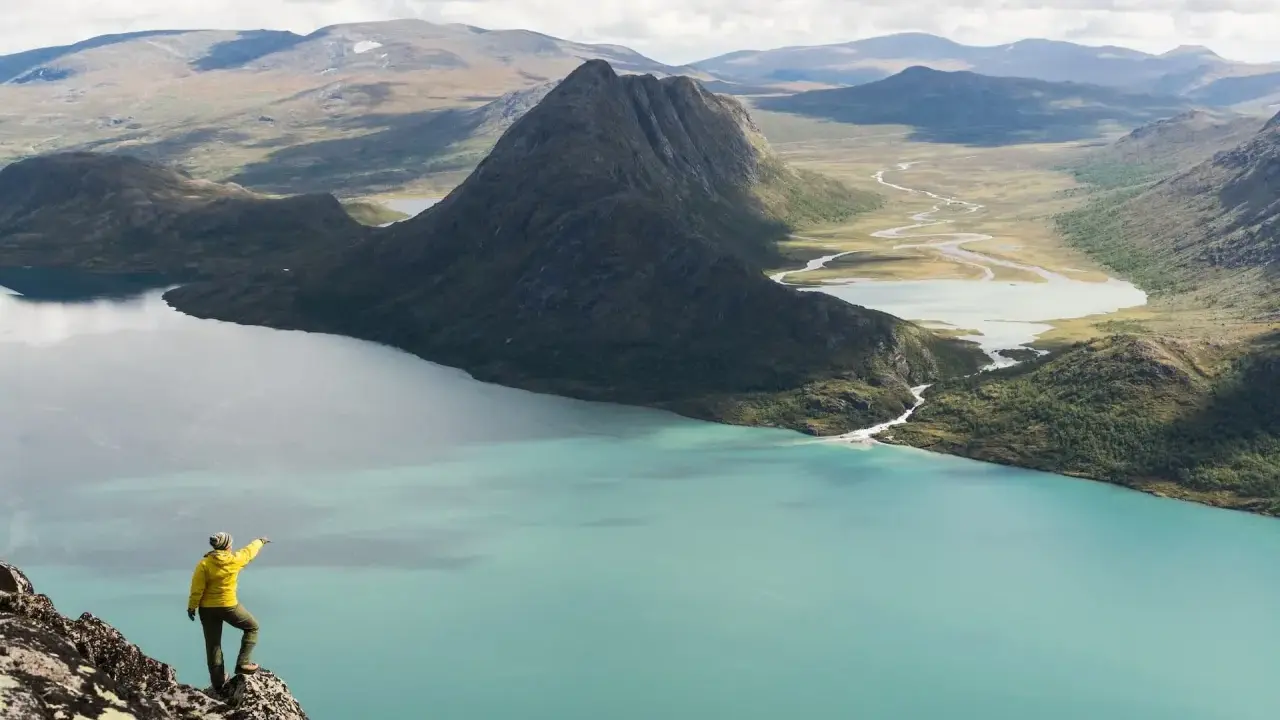 Vandrare pekar ut över turkost vatten och berg under en Besseggen vandring.