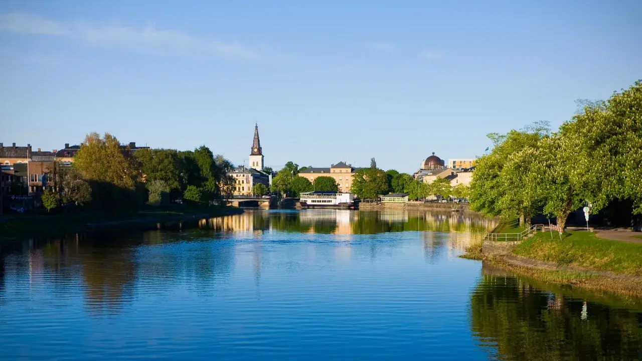 Vacker vy över Klarälven med stadens silhuett, kyrktorn och grönska. En perfekt plats att se i Karlstad en solig dag.