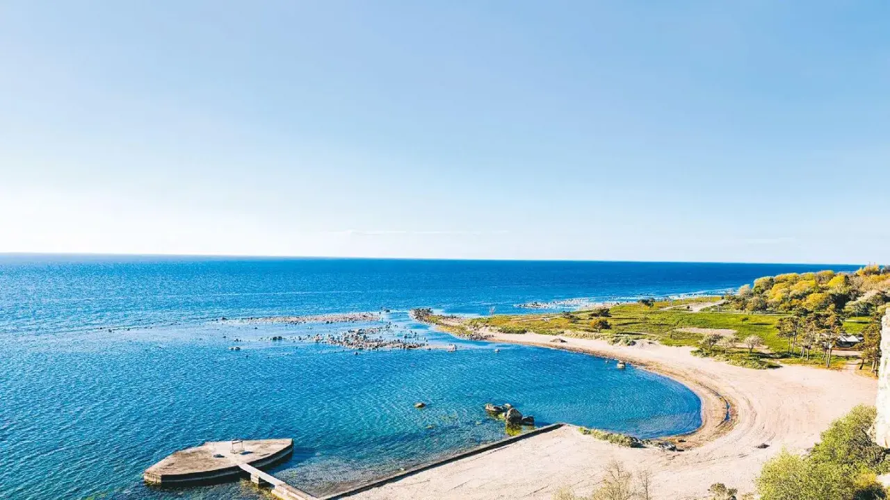 En vacker vy över ett vattenland på Gotland med en sandstrand, klart blått hav och gröna kullar.