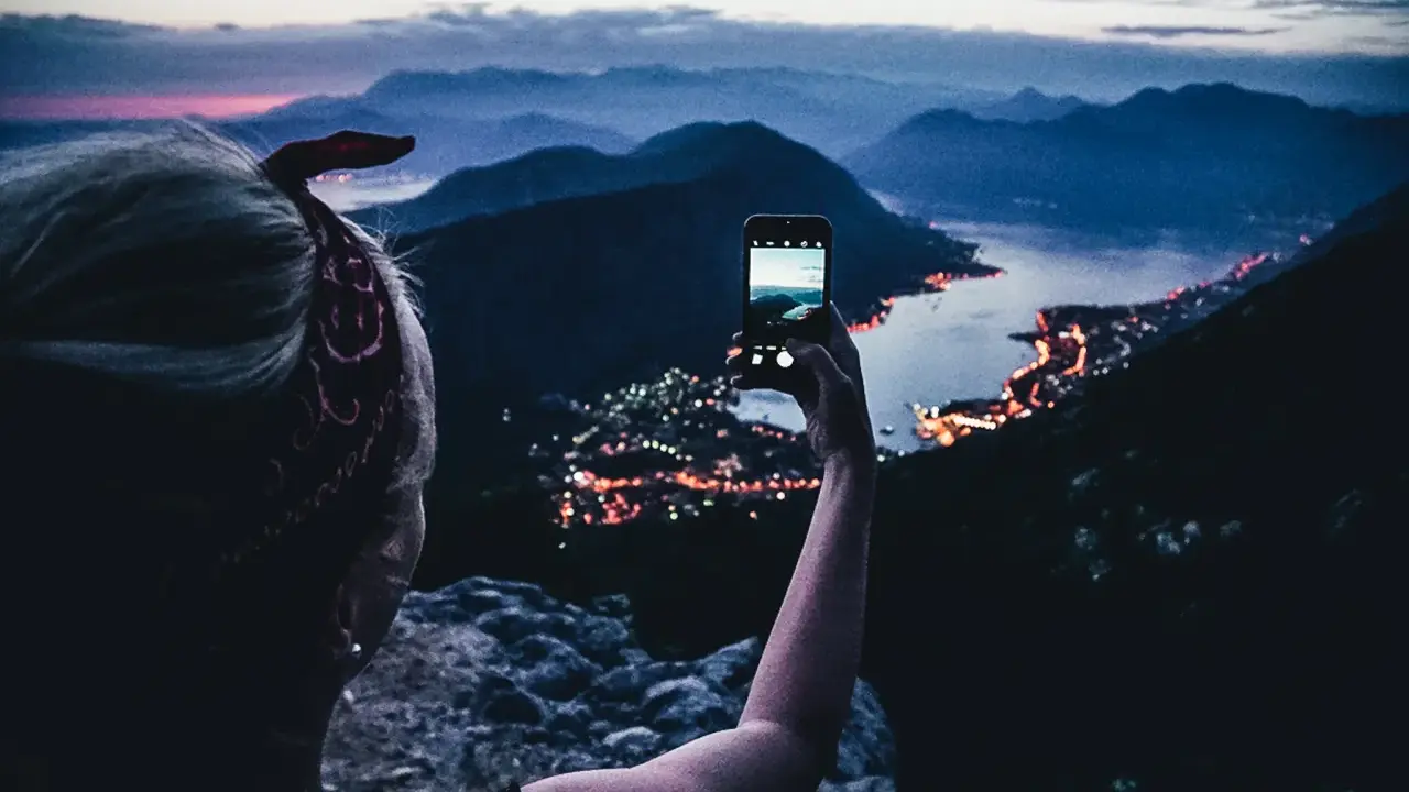 En person tar bild med mobiltelefonen av en stad vid havet i skymningen. En perfekt vy under en bilsemester Europa.