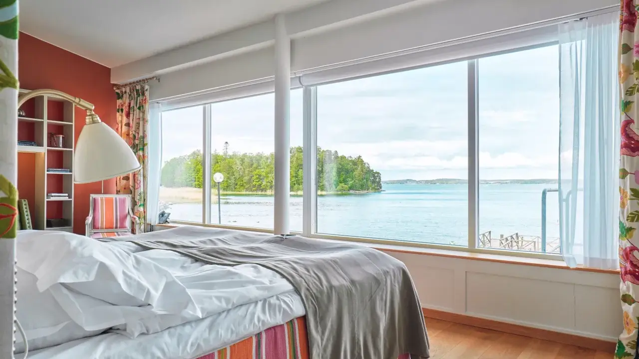 Sovrum med fantastisk havsutsikt, perfekt för ett bra hotell i Stockholm. Säng med vita lakan och grå pläd, färgglad randig sängkjol.
