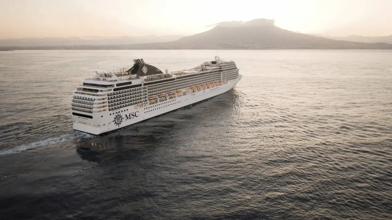 Kryssningsfartyget MSC Poesia glider fram på havet i solnedgången, med en vulkan i bakgrunden.