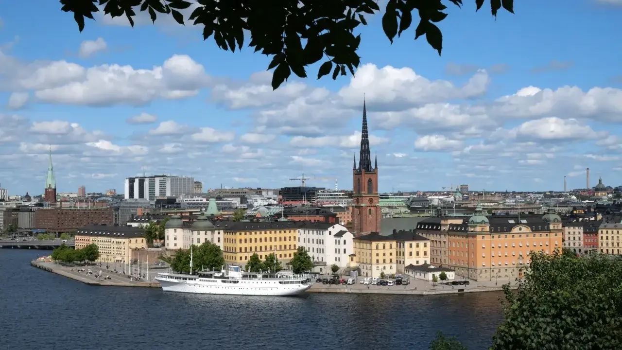 Vy över Riddarfjärden med en vit båt vid kajen, omgiven av Stockholms vackra byggnader. Perfekt för annorlunda utflykter i Stockholm.