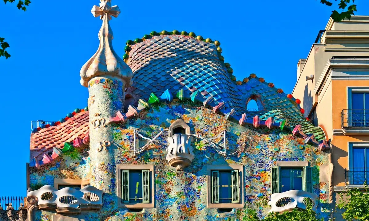 Färgglatt och fantasifullt **Gaudi hus Barcelona** med mosaiktak och unika balkonger under en klarblå himmel.