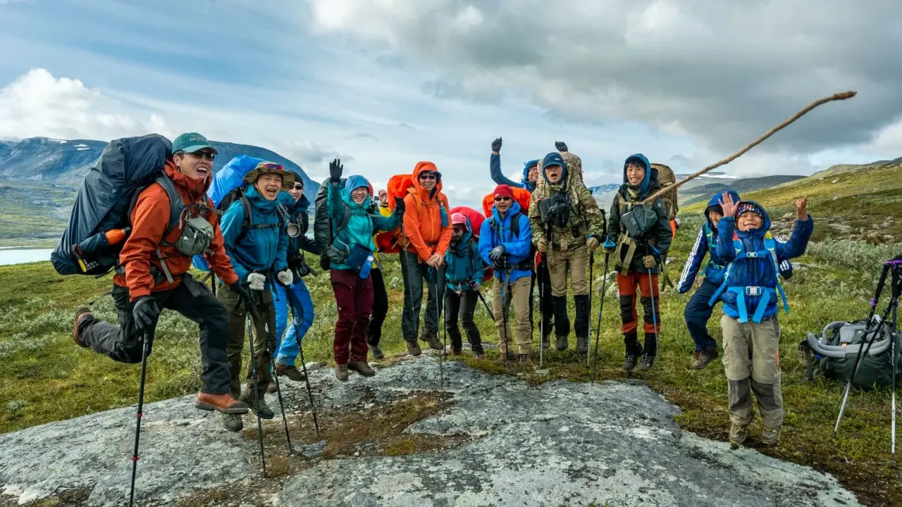Glada vandrare, redo för Fjällräven Classic i svenska fjällen. De hoppar av glädje på en sten.