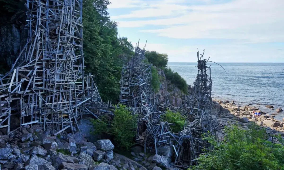 Nimis i Skåne: en skulptur av trä som klättrar uppför klipporna vid havet.