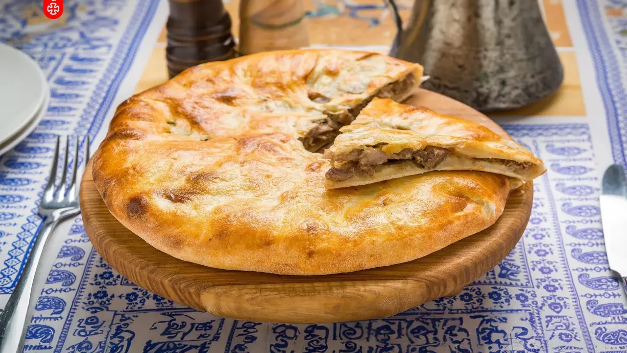 En gyllene, nybakad khachapuri, en klassisk georgisk mat, ligger på en träskärbräda. En bit är uppskuren och visar det smakrika köttfyllningen.