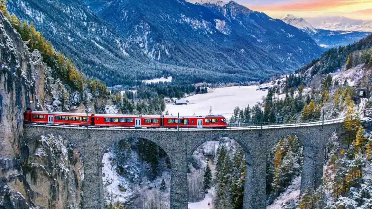 Röda tåget korsar en stenbro över en snöig dal i Schweiz. Fantastiska vyer för din resa till Schweiz tips.