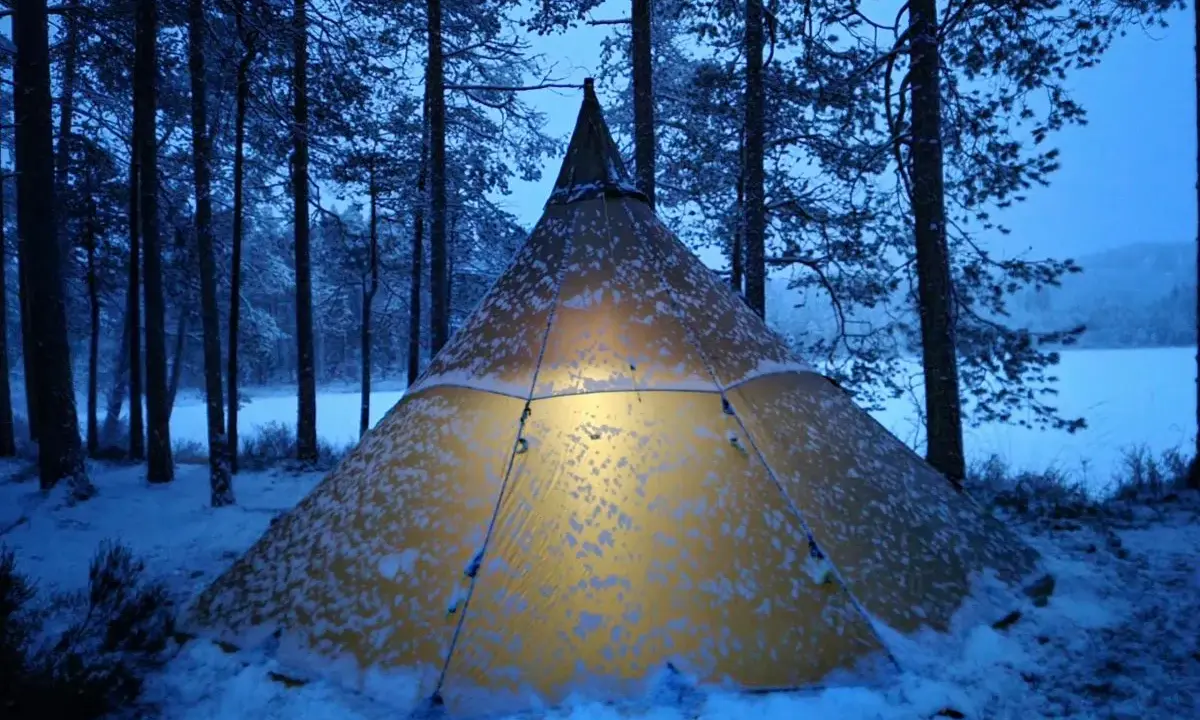 Varmt ljus lyser från ett snötäckt tält i Glaskogens naturreservat. En magisk vinterkväll.