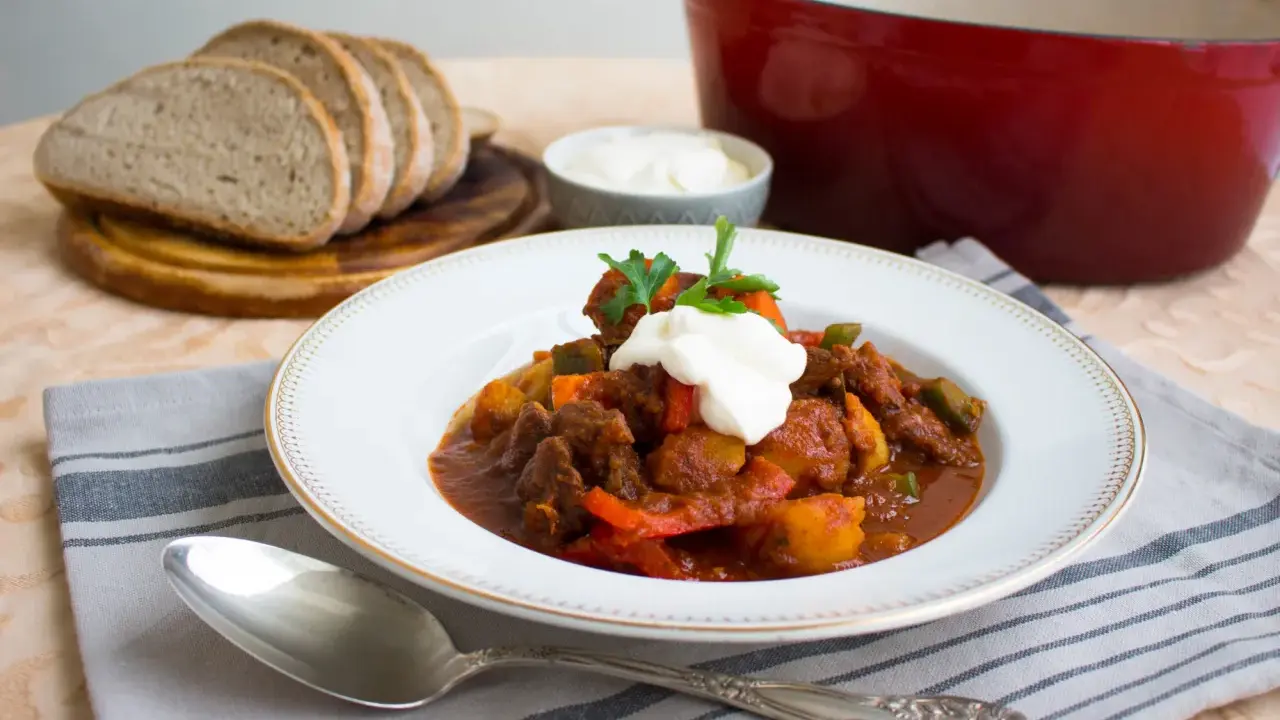 En portion mustig ungersk mat, en mustig gryta med kött och grönsaker, toppad med gräddfil och persilja. Serveras med gott bröd.