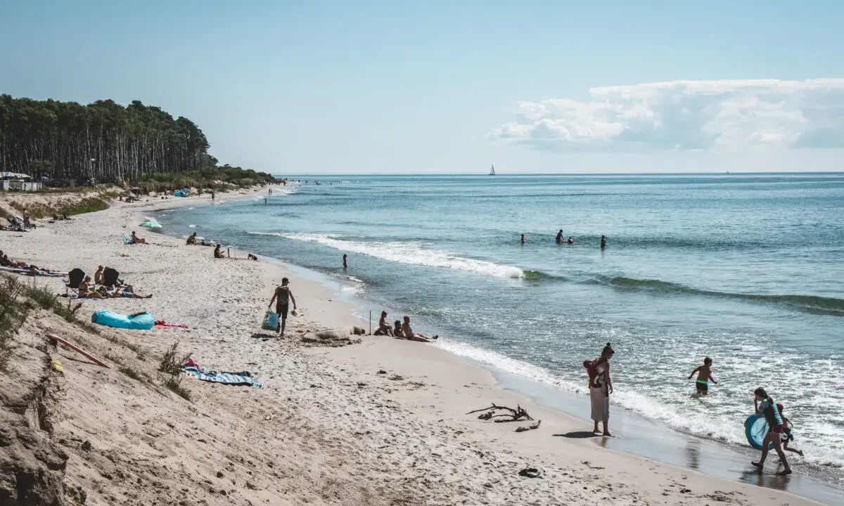Människor njuter av solen och havet på sveriges finaste strand. Barn leker i vattnet medan andra kopplar av på sanden.
