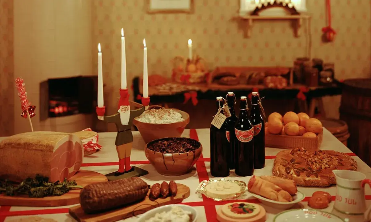 Julbord i Sverige med julmat som skinka, korv, risgrynsgröt och julmust. En tomte ljusstake lyser upp bordet.