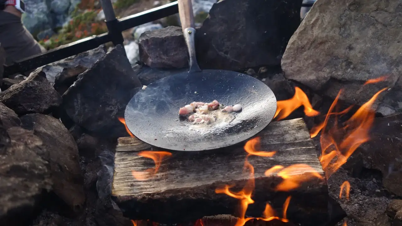 Stekt fläsk i stekpanna över öppen eld, en del av ett recept kolbullar. Elden sprakar och röken stiger.