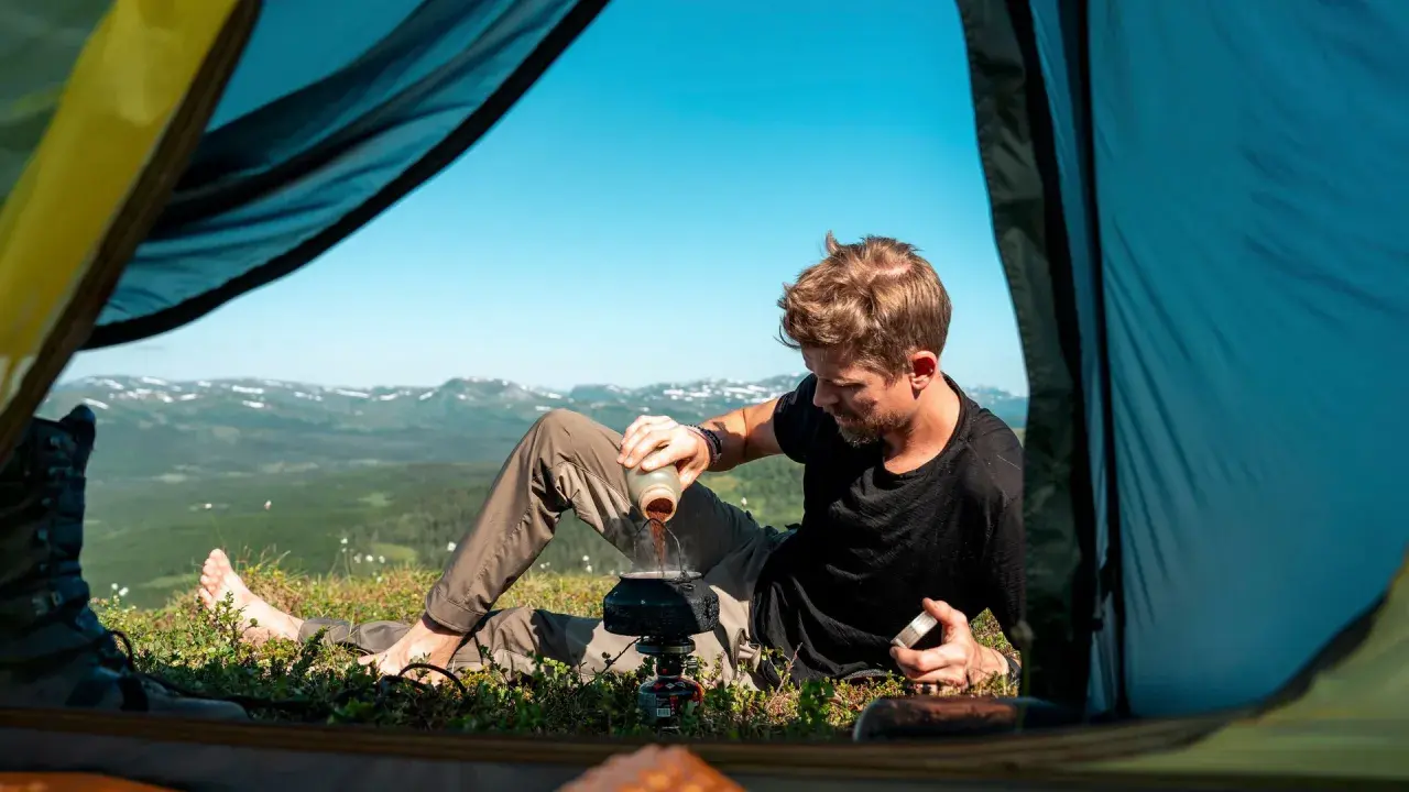 Man gör kaffe vid tältöppningen under en vandring i Sverige sommar. Vacker utsikt över fjällen.