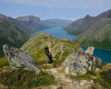 En kvinna vandrar i Jotunheimen med en blå sjö och berg i bakgrunden. En T-märkt sten visar vägen.