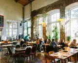 Folk äter och dricker på en livlig restaurang i Tallinn. Stora fönster släpper in solljus i lokalen med rustika tegelväggar.