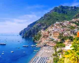 Färgglada hus klättrar uppför bergssluttningen vid en livlig strand och blått hav. En vacker vy som ger fakta om Italien.
