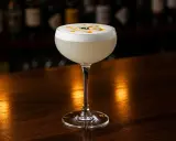 En elegant Pisco Sour med skummig topp, dekorerad med en virvel och tre svarta bär. Perfekt för ditt pisco sour recept.