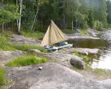 En liten segelbåt med åror ligger vid en stenig strand. En härlig plats att paddla Dalslands kanal på.