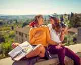 Två glada vänner njuter av sin resa i Europa, med en karta och kamera redo för nya äventyr i en vacker italiensk landskapsvy.