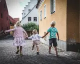 Tre barn håller varandra i handen på en kullerstensgata på Gotland, på väg mot äventyr.