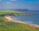 Grönskande kullar och en sandstrand vid havet på Irland, nära Belfast.