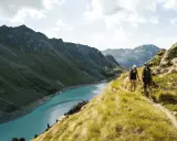 Två personer vandrar på en bergstig med en turkos sjö och dramatiska berg i bakgrunden. En perfekt dag för att vandra i Schweiz.