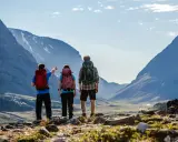 Två vandrare med ryggsäckar blickar ut över en dal under en kungsleden vandring. En pekar mot bergen.