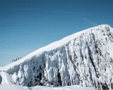 En grupp vandrare på en snöig bergstopp under en helags topptur. Den isiga bergväggen reser sig dramatiskt mot en klarblå himmel.