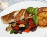 Pan-seared fish with roasted vegetables, a grilled lemon slice, and basil on a white plate.
