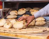 En hand tar färskt, fluffigt bröd från en ugn. Detta är en del av den autentiska egyptiska maten, perfekt för att doppa i läckra röror.