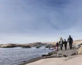 Familj promenerar längs en stenig strand vid Tjurpannans naturreservat.