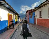Färgglada hus i La Candelaria, Bogotá. En kvinna med ryggsäck går längs en kullerstensgata. Här finns fakta om Colombia.
