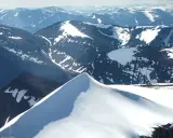 En grupp vandrare närmar sig toppen av Kebnekaise, Sveriges högsta berg. Snöklädda bergskedjor sträcker sig mot horisonten.