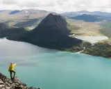 Vandrare pekar ut över turkost vatten och berg under en Besseggen vandring.