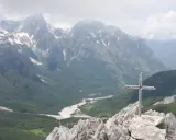 Kors på en klippig topp med en dal och snöklädda berg i bakgrunden, en vy över norra Albanien.